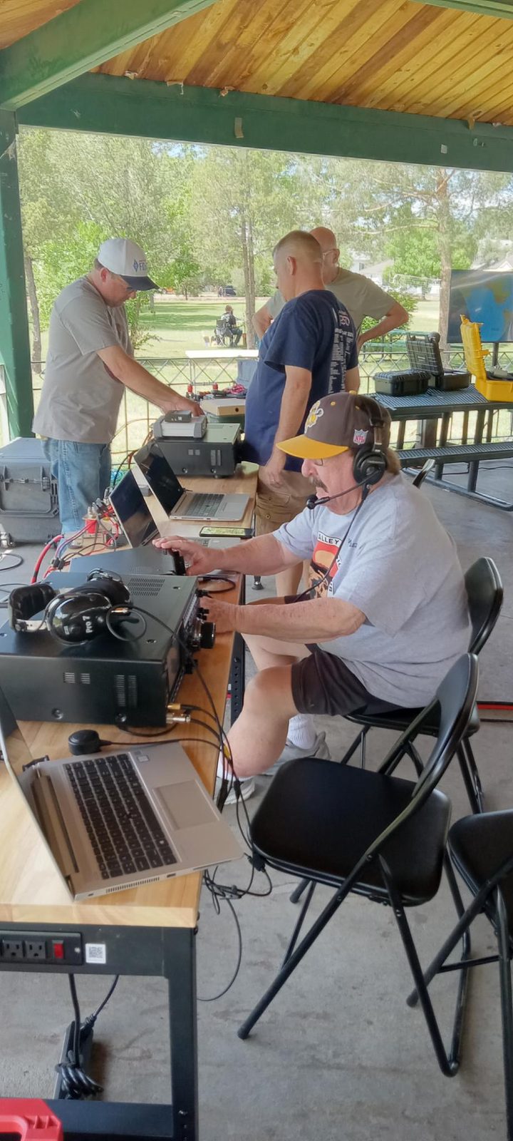 One member coaching another at a radio under the gazebo.