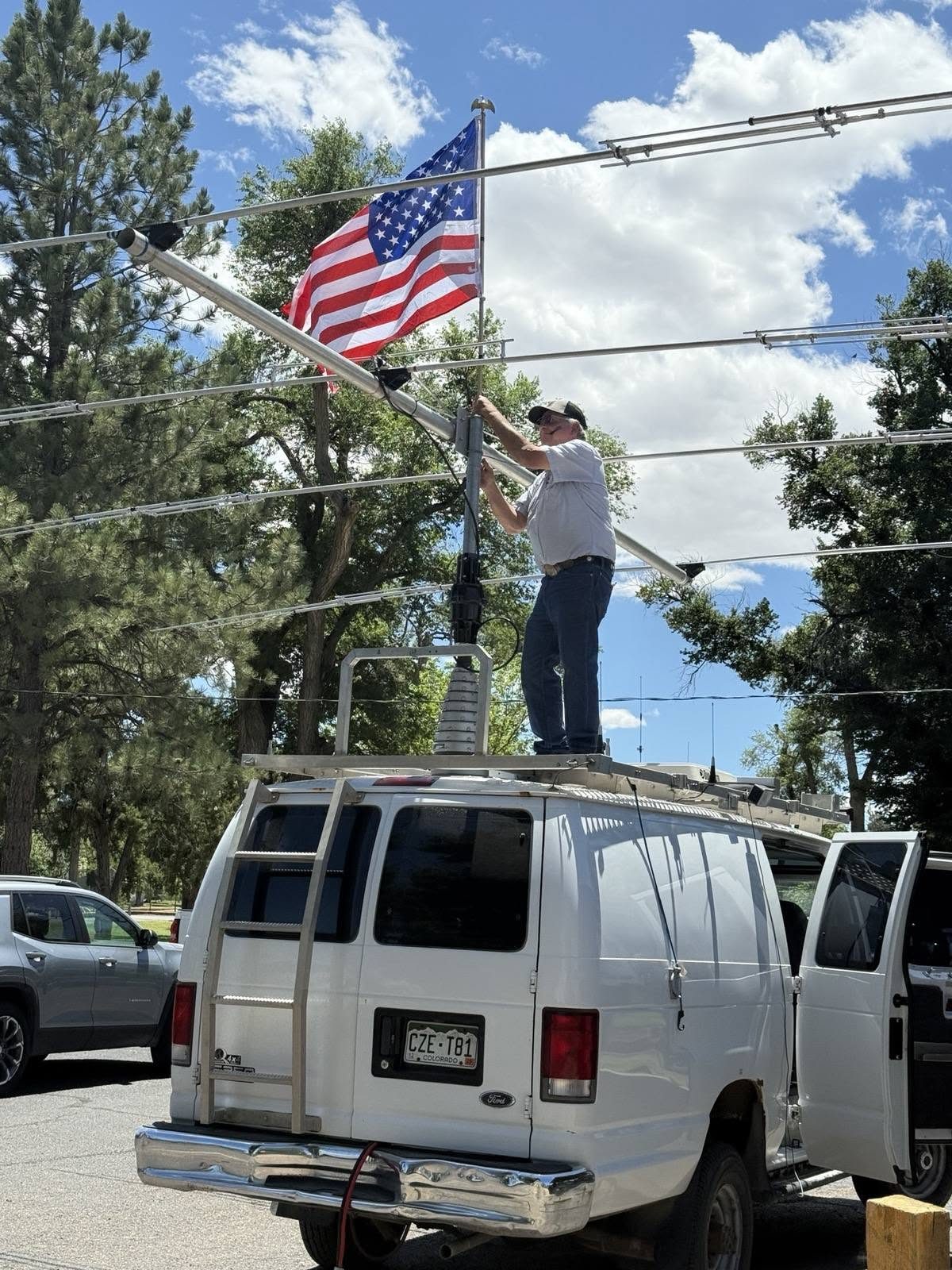 Club members raise the antenna mast from the roof of the EOC van, American flag flying from the mast.