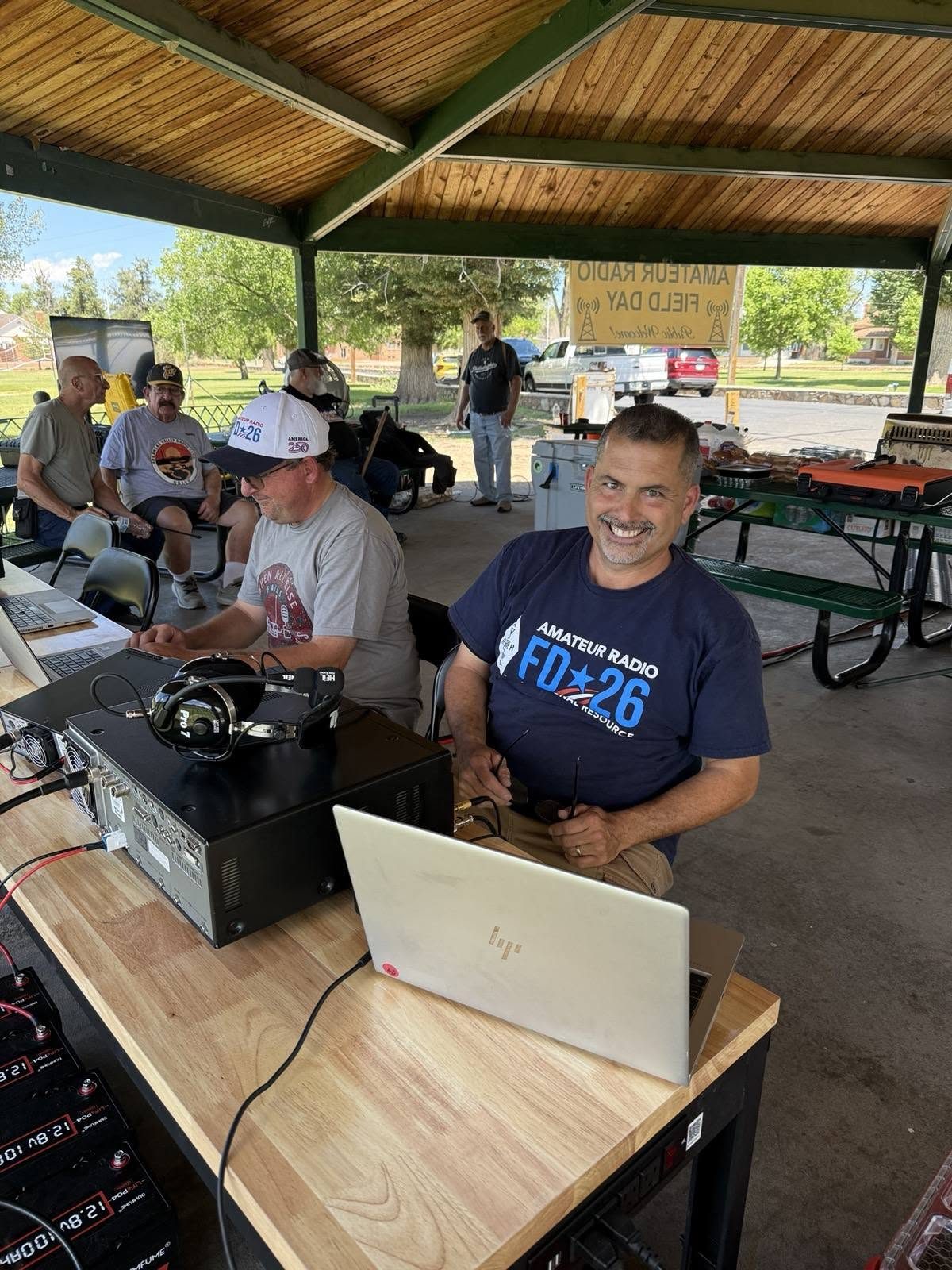 Operator in a Field Day 2026 shirt working a station, transceiver and laptop on the table.