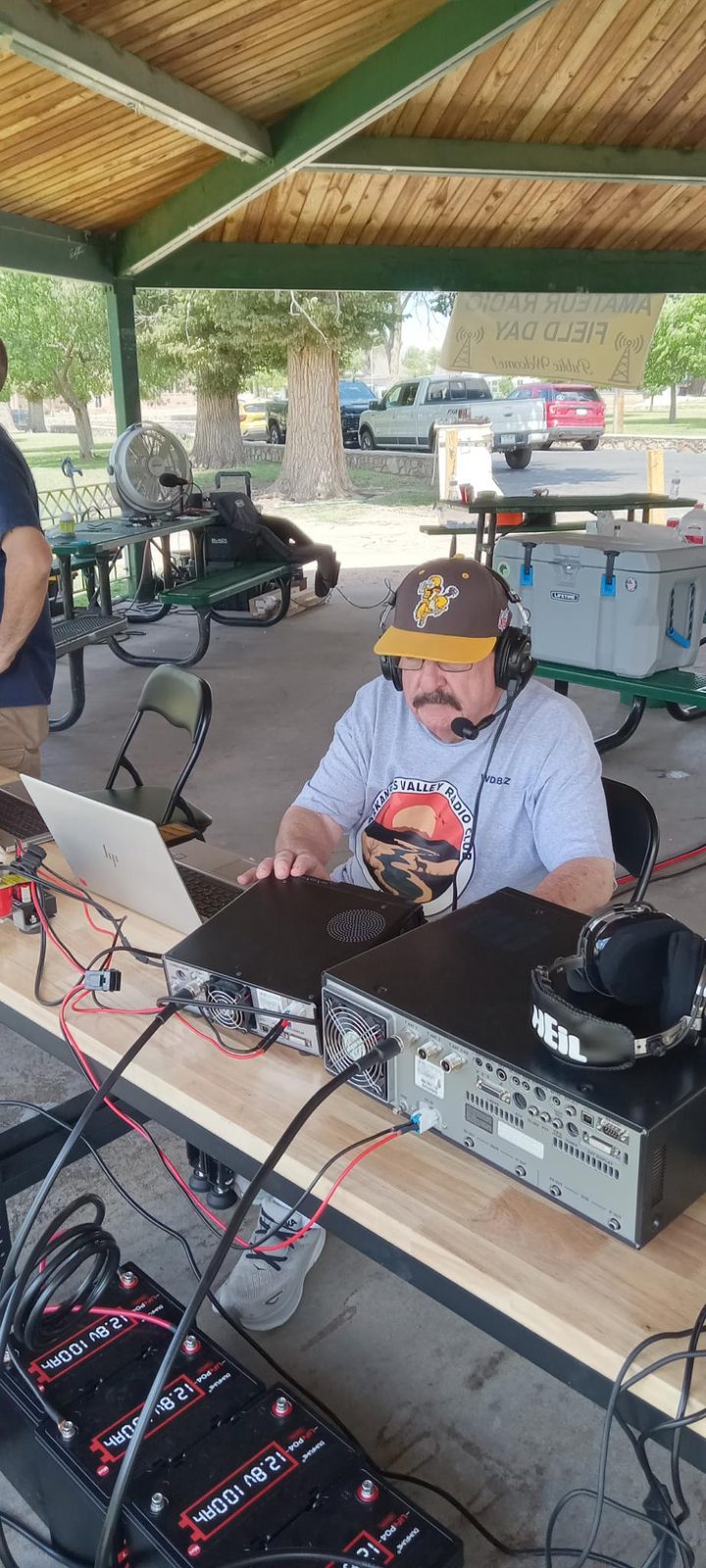 Operator at an HF station under the gazebo, logging contacts on a laptop.